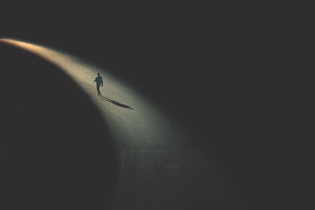Illustration of single person walking on a path of light against a dark, foreboding background.